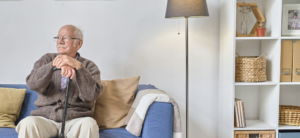 Elderly man sitting on blue sofa with cane